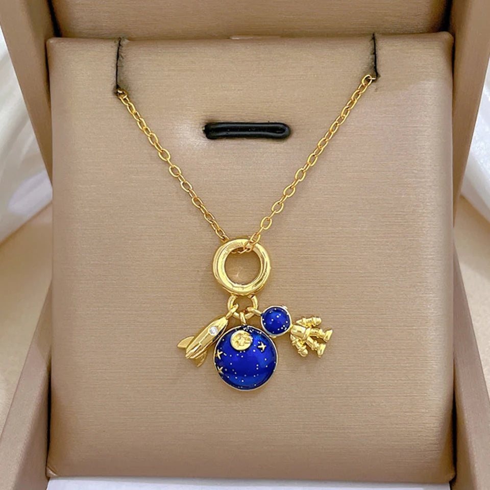 Gold-tone charm necklace with rocket, blue planet and astronaut charms in a gift box