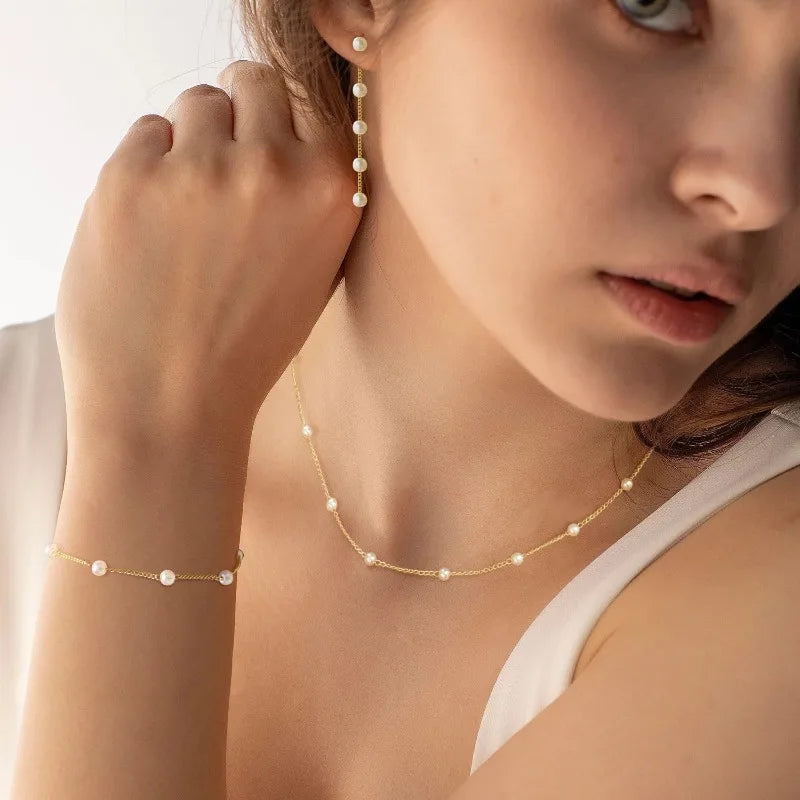Close-up of dainty gold plated pearl station necklace and bracelet on model