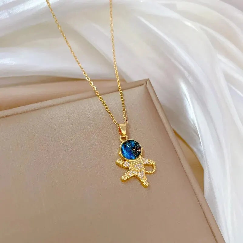 Gold-tone astronaut pendant necklace with a blue planet stone on cream fabric