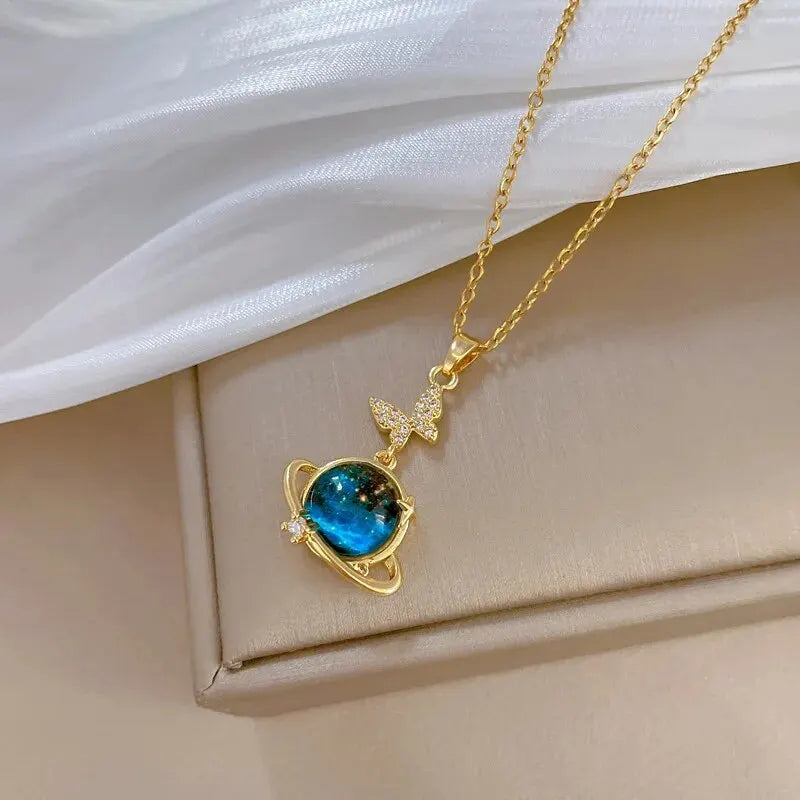 Gold-tone planet pendant necklace with a blue stone and butterfly accent on a gift box