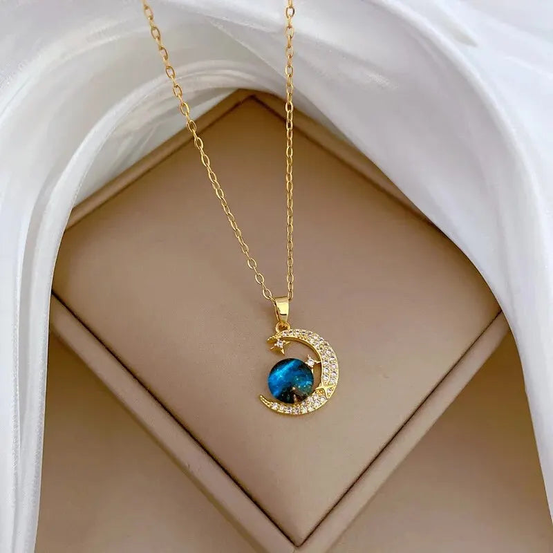 Gold-tone crescent moon and blue planet pendant necklace shown in a gift box