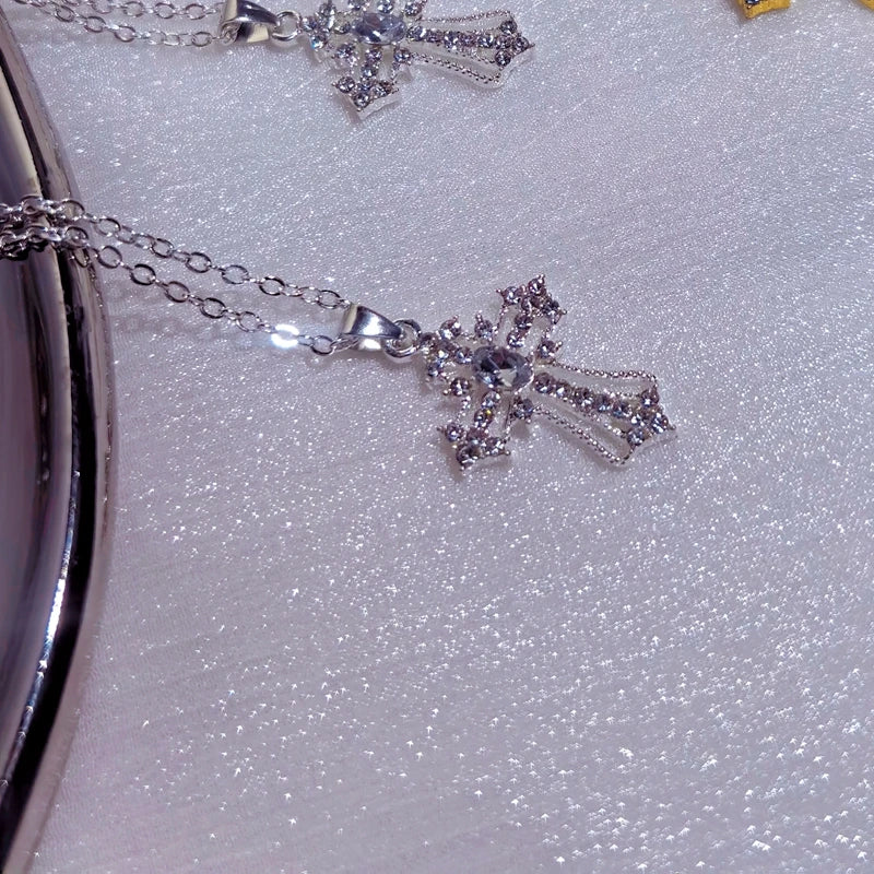 Silver cross pendant necklace with clear crystals resting on a lilac glitter surface