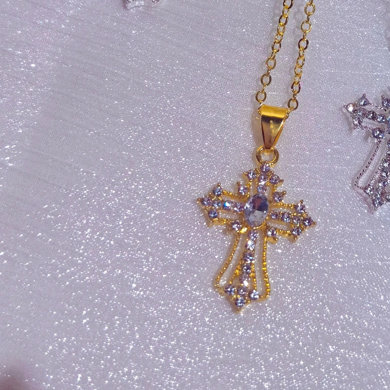 Gold tone cross pendant necklace with purple and clear rhinestones on a lilac glitter surface