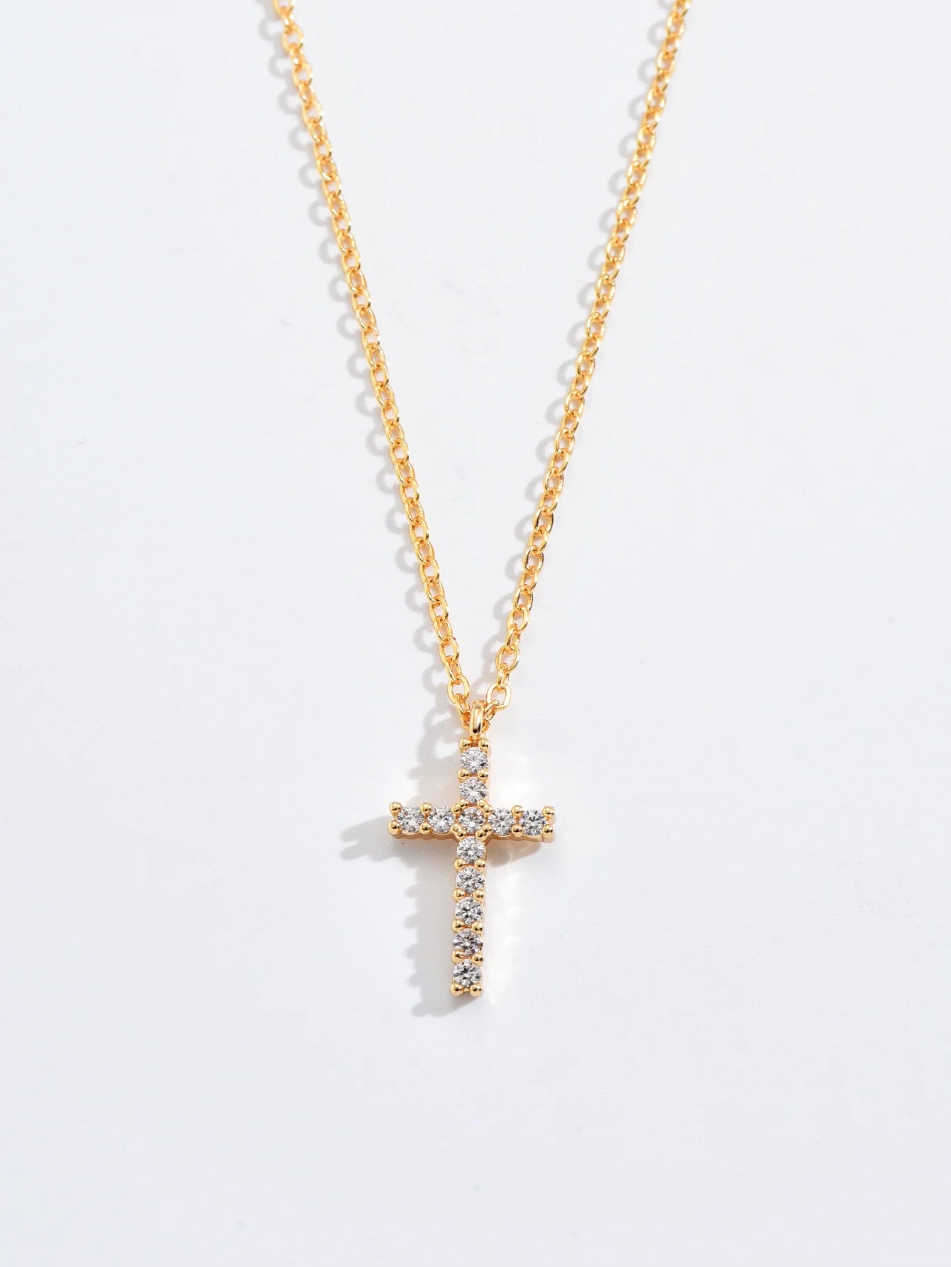 Macro view of the gold-tone cross pendant showing the pave-set zircon stones