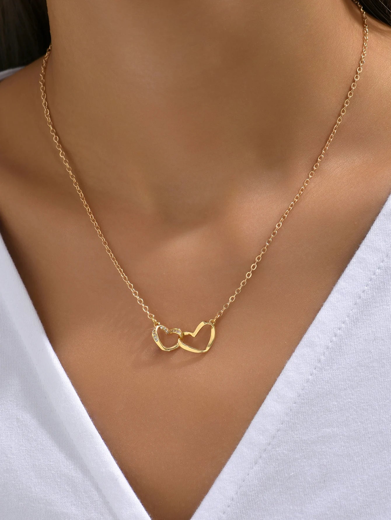 Woman in a white V-neck top wearing the gold-tone double heart necklace