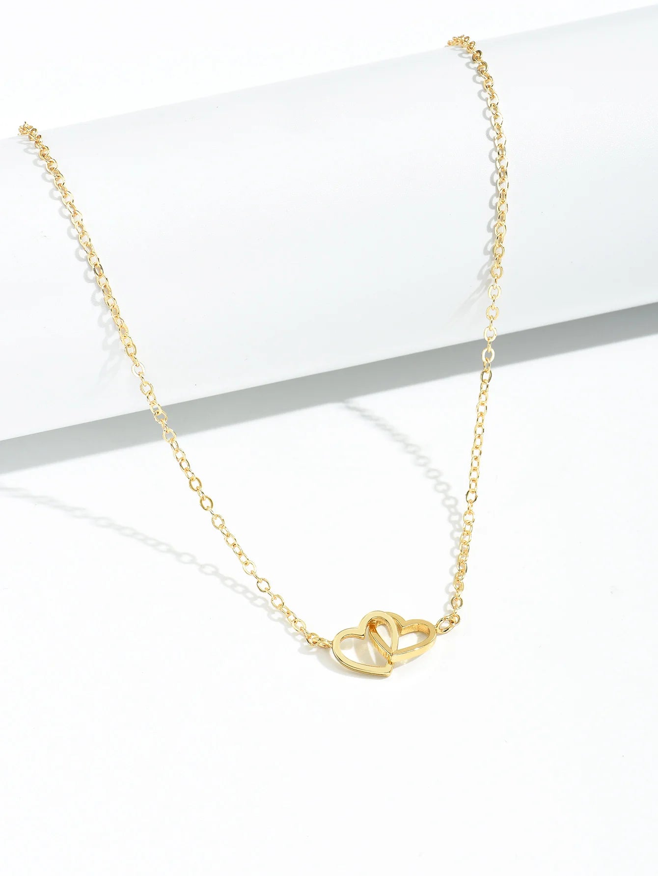 Gold-tone double heart pendant necklace draped over a white block on a white background