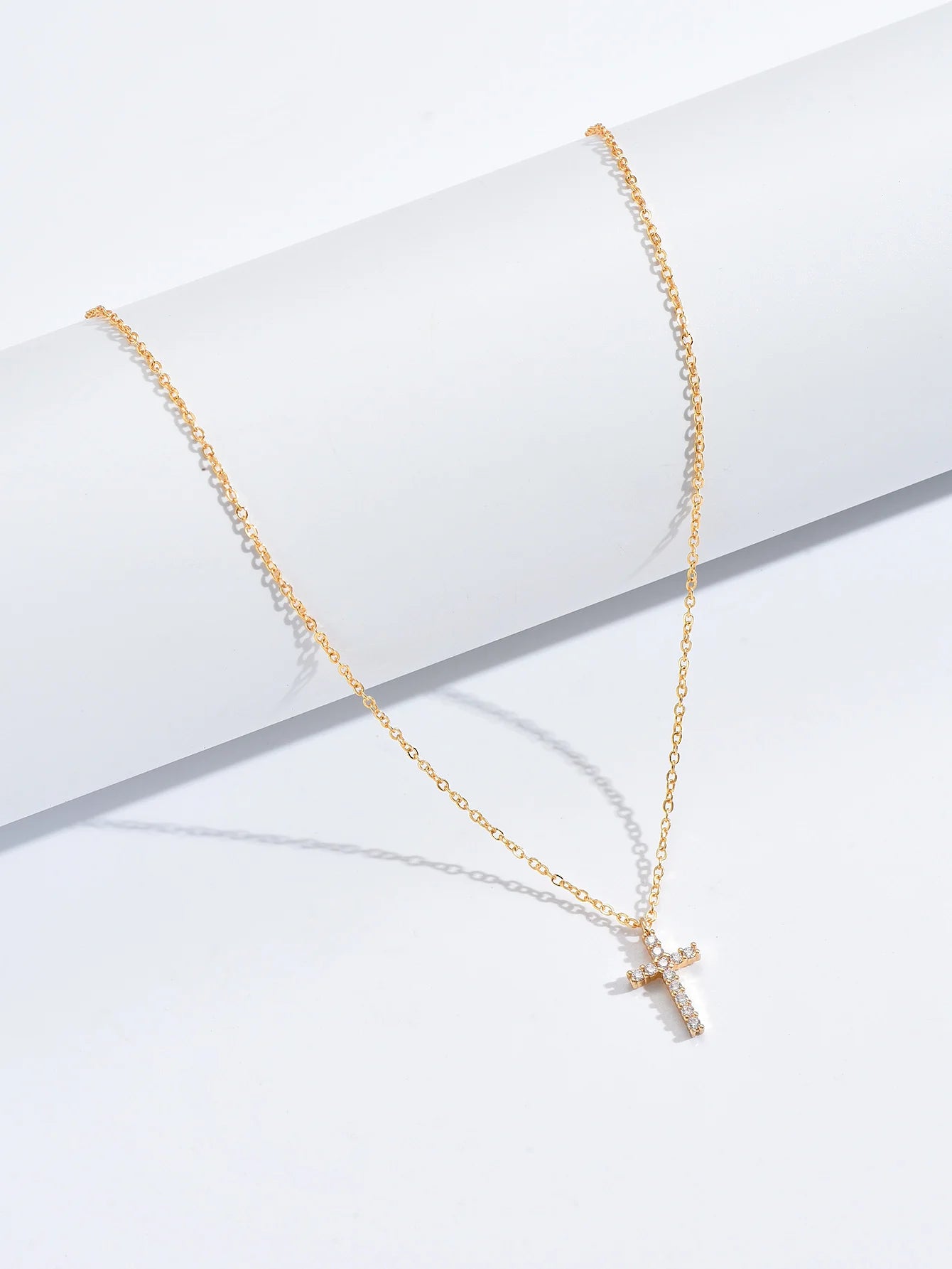 Gold-tone link chain and zircon cross pendant draped over a white display cylinder