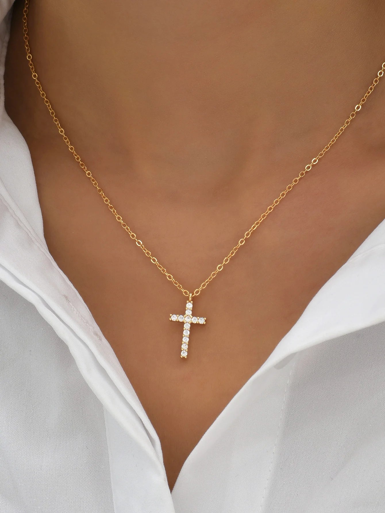 Gold-tone zircon cross pendant necklace worn with an open white shirt