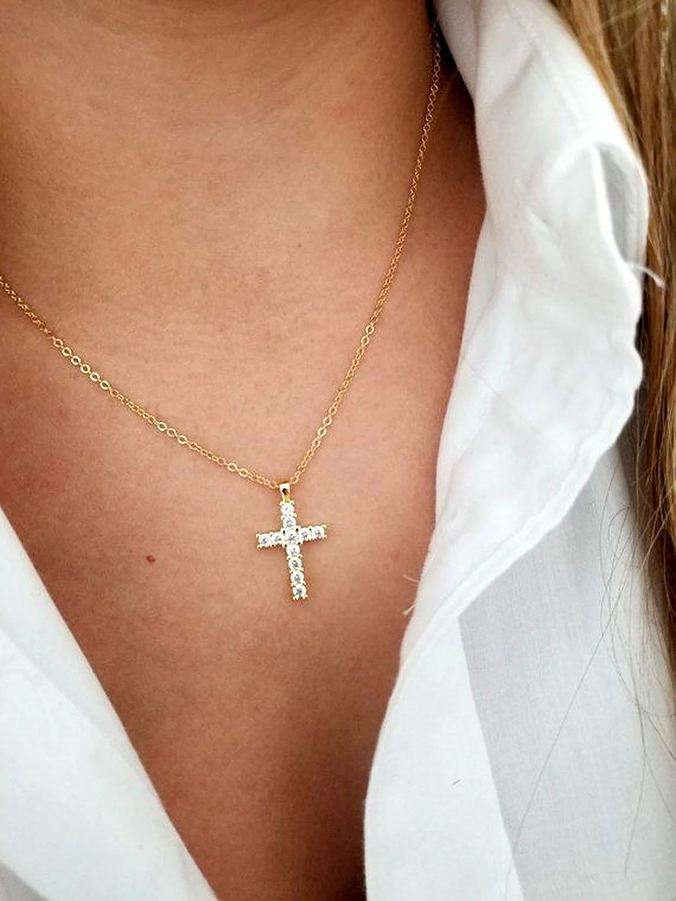 Close-up of the gold-tone zircon cross pendant resting below the collarbone