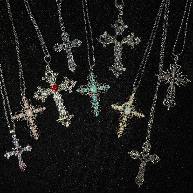 Collection of gothic cross pendant necklaces in silver, gold and colored rhinestones laid out on black fabric