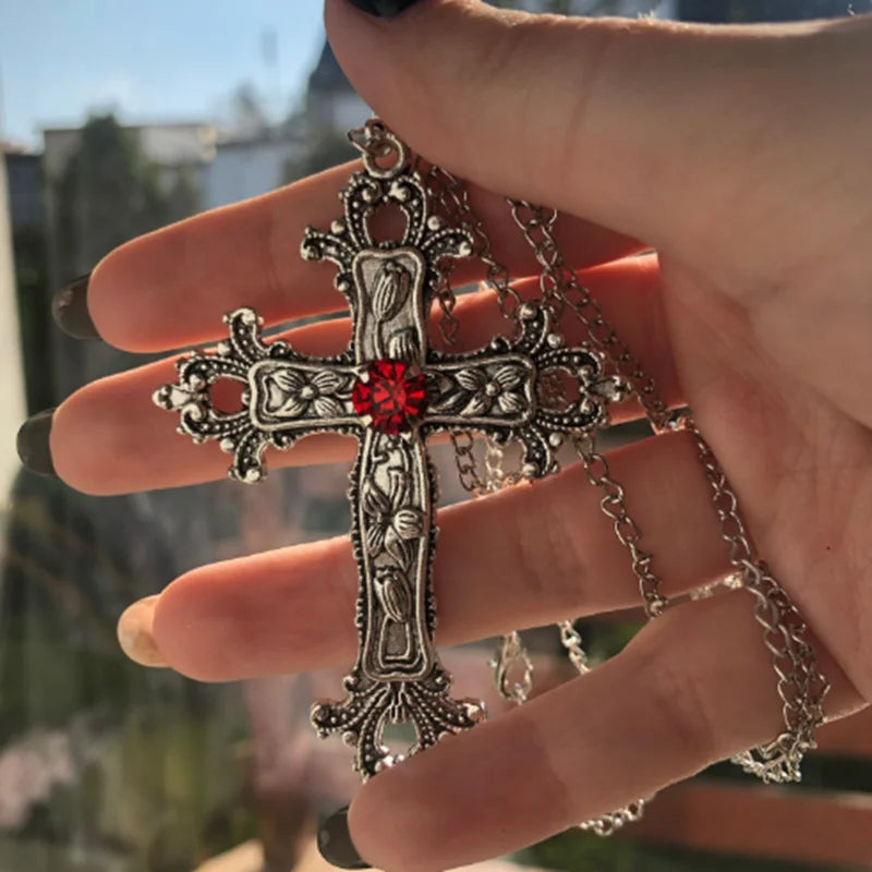 Large silver gothic cross pendant with a red center stone held in a hand to show its size
