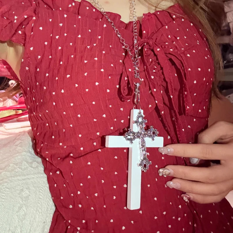 Woman in a red polka dot dress wearing the large cross pendant necklace layered on a fine chain