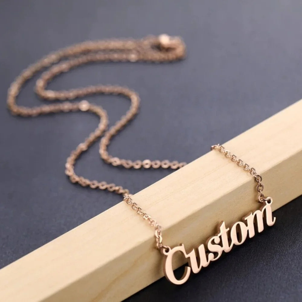 Rose gold-tone personalized name necklace spelling Custom draped over a wooden block