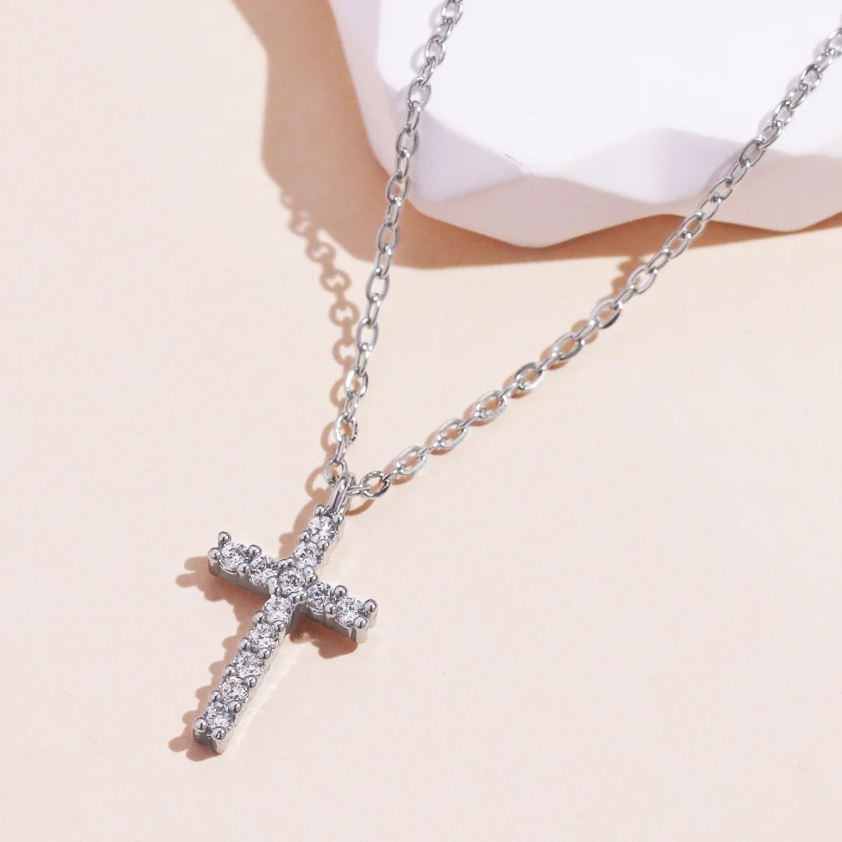 Silver-tone zircon cross pendant necklace on a cream background